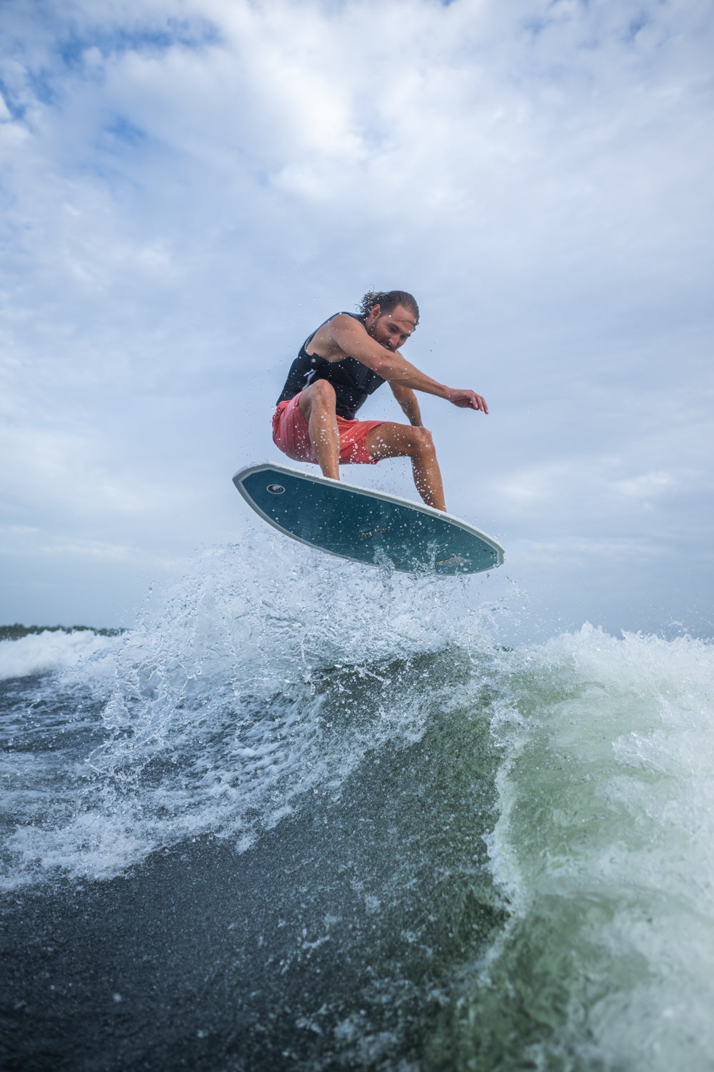 A male wakesurfer catches air on the Bentley board, lifting above the wave with water spray surrounding him.