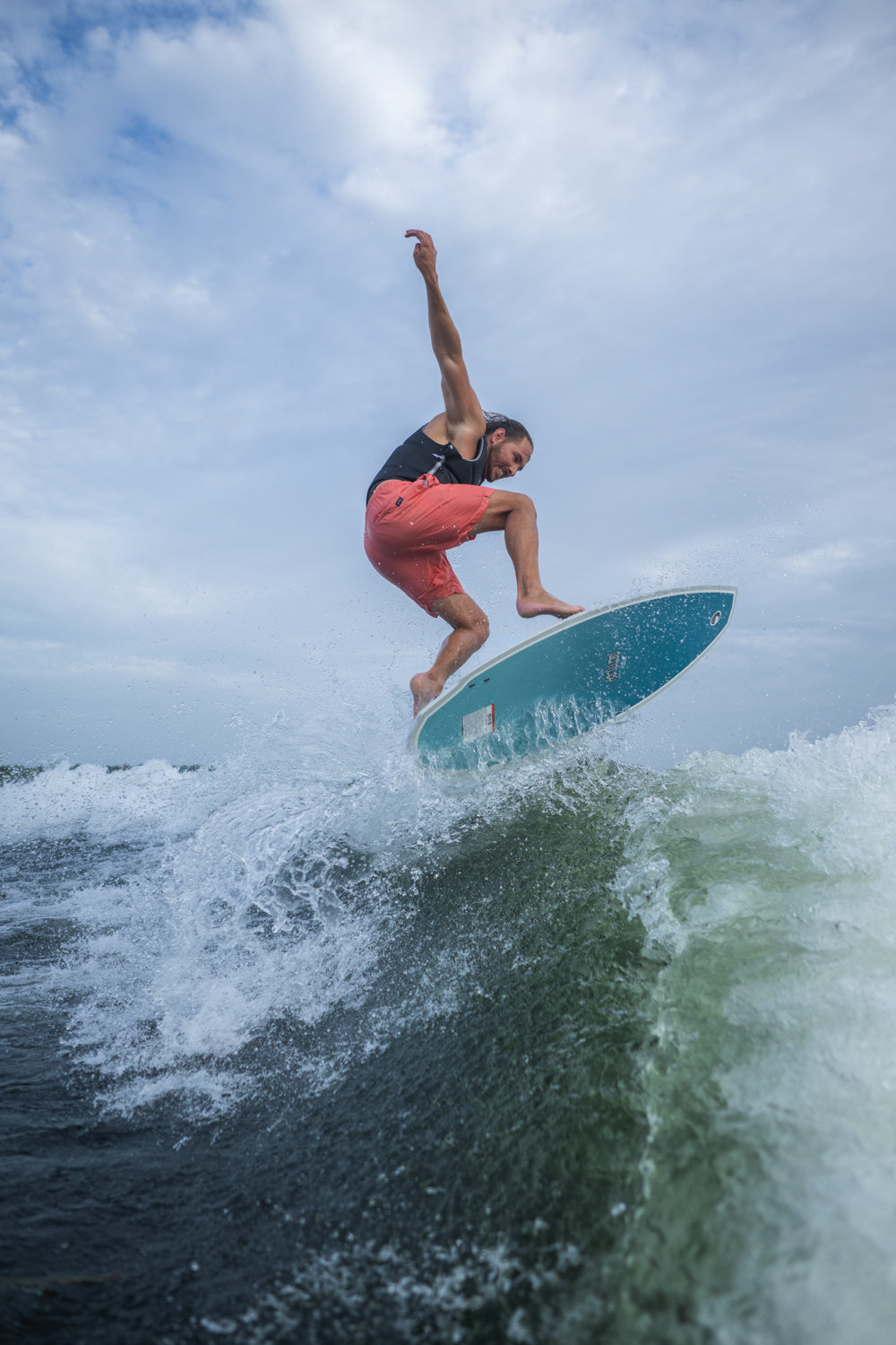 A male rider carves through a wake on the Bentley wakesurf board, maintaining balance with water splashing around him.