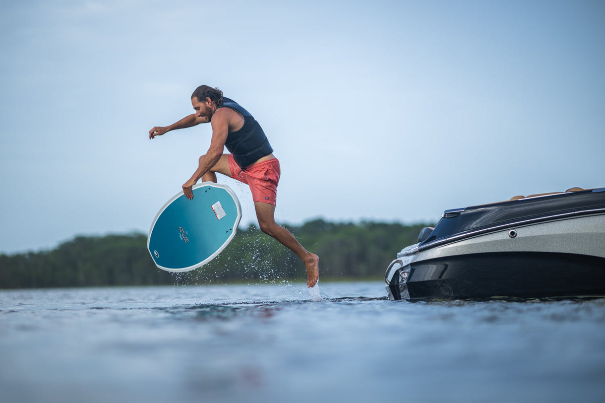 A male wakesurfer leaps off a boat‚Äôs platform onto the Connelly Bentley wakesurf board, preparing to ride the wave.