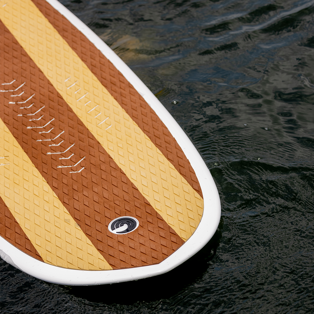 Close-up of the Big Easy wakesurfer‚Äôs textured deck with brown and yellow stripes floating on the water.