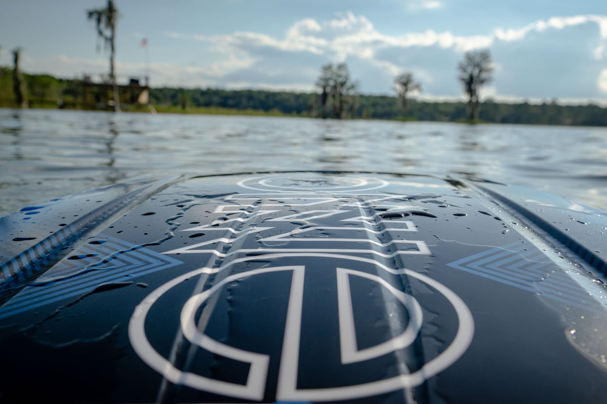 Close-up of the Boost kneeboard partially submerged in water, showcasing its glossy black and blue design details.