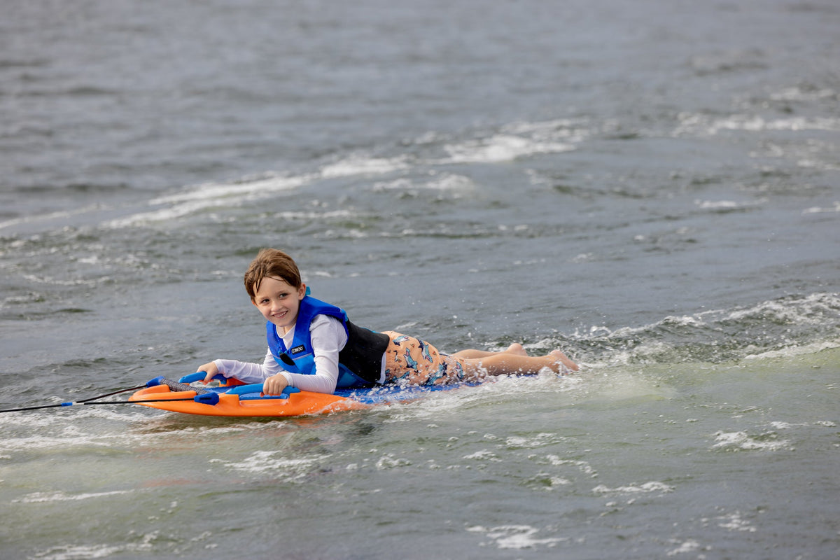 Child smiling on a Wild Thing orange kneeboard with handles, wearing a life vest.