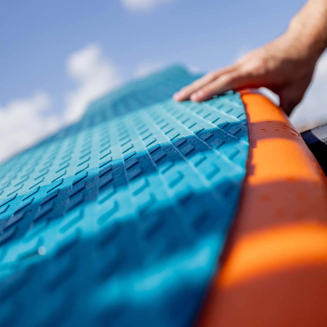 Close-up of a textured blue grip pad on the Cloud 9 orange wakesurfer, with a hand resting on the edge.