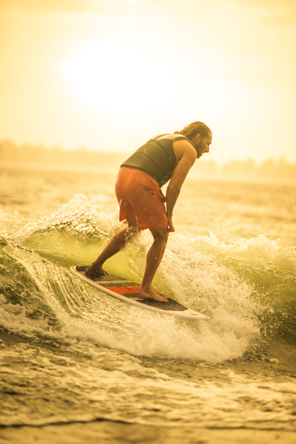 A rider carving on the HABIT Skim wakesurf board at sunset, creating a spray of water while maintaining balance.