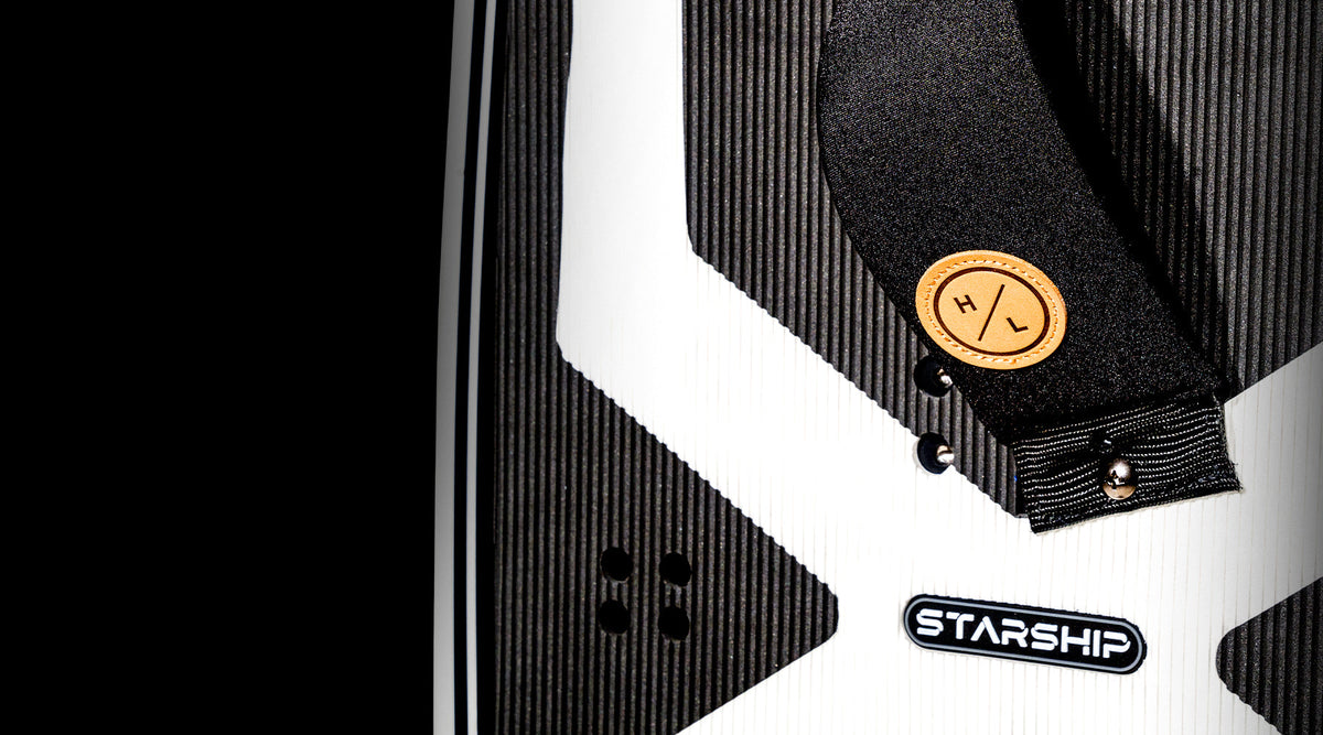 Close-up of a black & white Starship 3.4 surfboard with logo and strap detail.