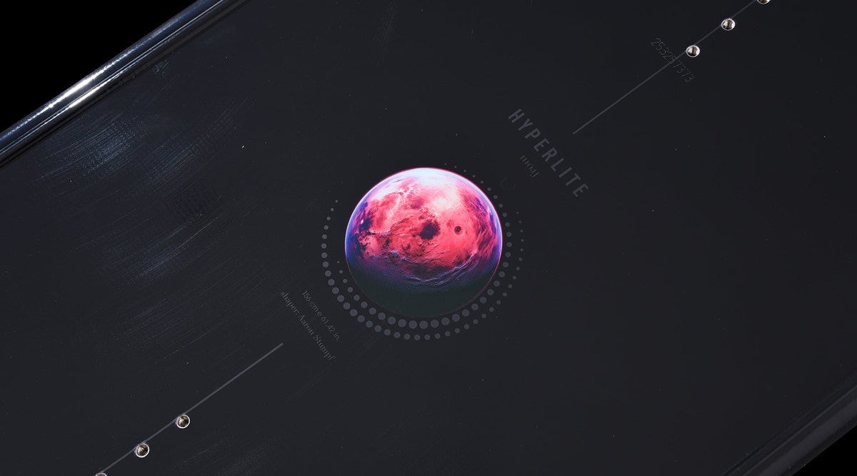 Close-up of pink planet graphic detail on the black deck of the Pleasure wakeboard.