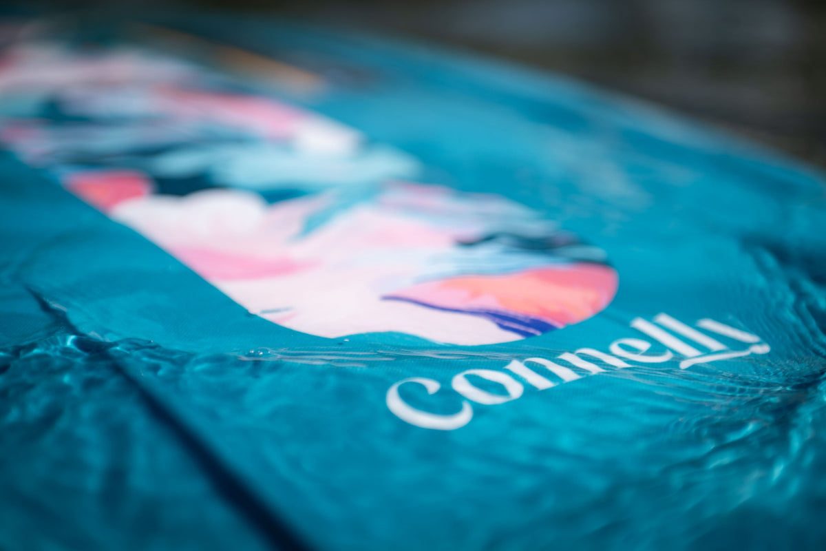Close-up of the Lotus wakeboard‚Äôs surface, showing a blue and pink marbled graphic with the Connelly logo in water.