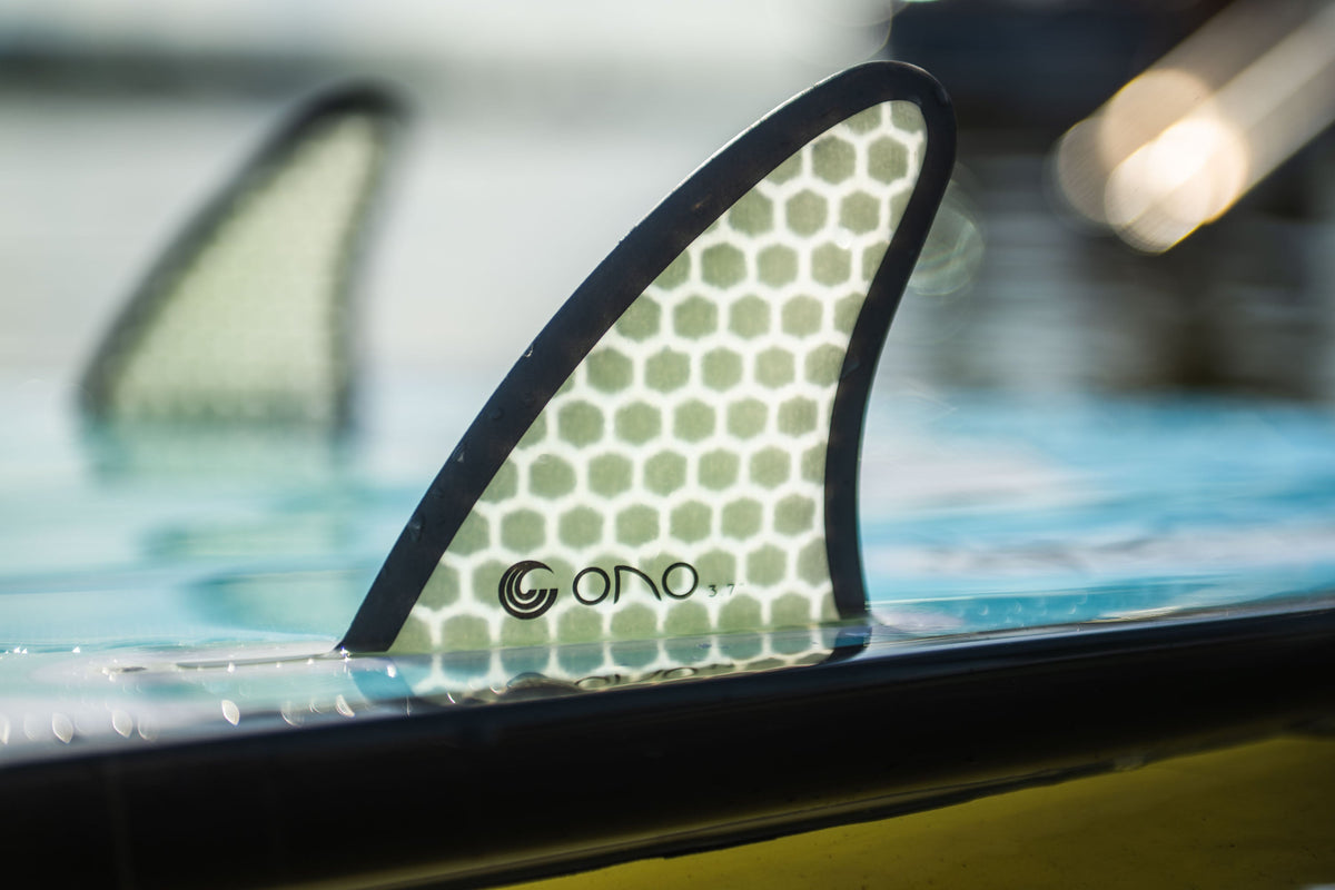 The Ono wakesurf board‚Äôs fin with a honeycomb design is partially submerged in water.