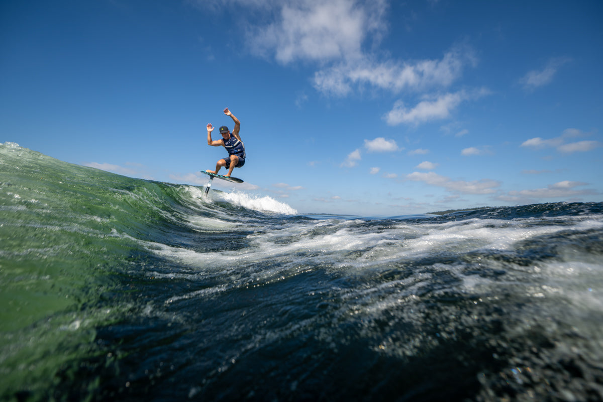 Surfer riding the Shuttle w/Falcon Foil Kit & Trainer Mast under a clear blue sky.