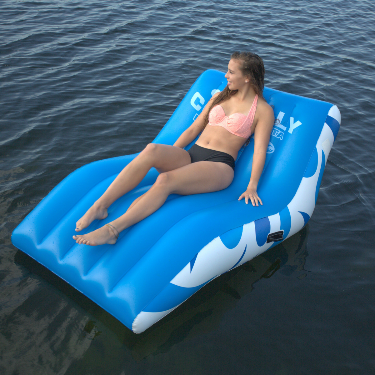 Lifestyle view of a woman reclining on the Party Cove Siesta on water with its ergonomic shape and cushioned support.